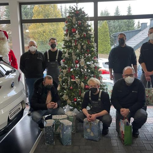 Mitarbeiter mit Geschenktüten vor Weihnachtsbaum